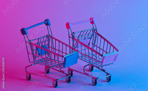 Two shopping trolley in trendy neon light. Gradient pink-blue glow. Concept art. Minimalism