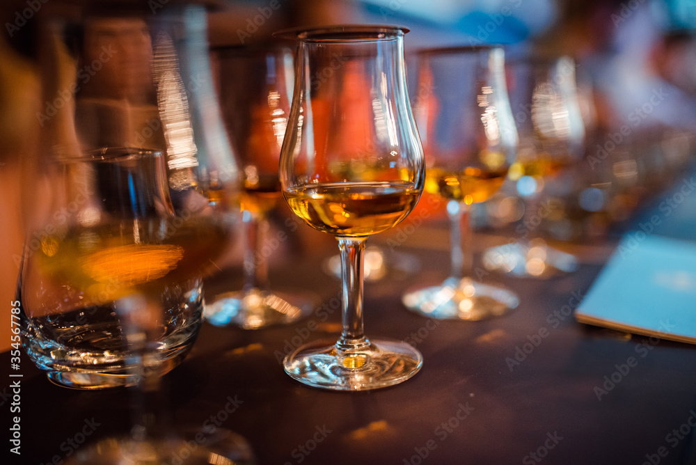 Glasses with brandy stand in a row. Blurred background, warm tinted. Tasting glasses with aged french cognac brandy