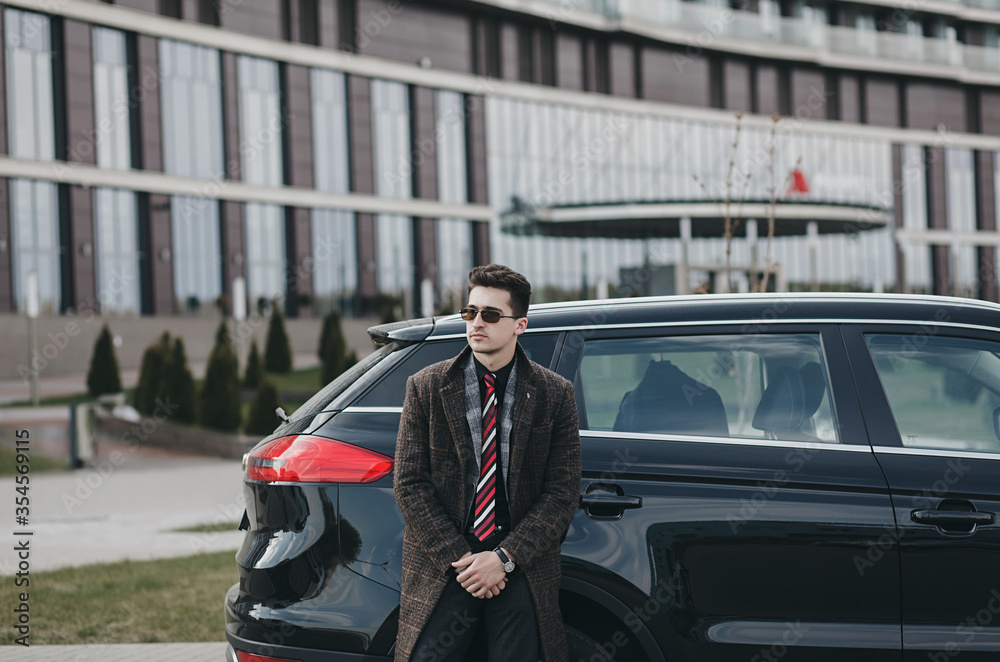 handsome man in a coat stands next to a new car.