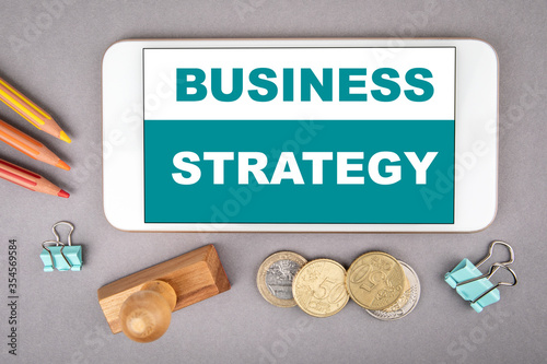 BUSINESS STRATEGY concept. White mobile phone, colored pencils and wooden stamp