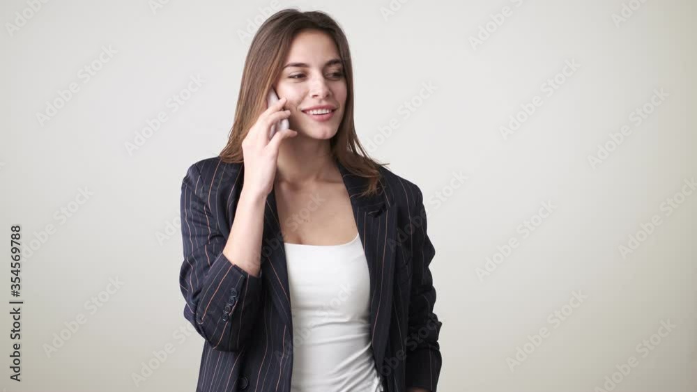 A beautiful young woman wearing casual clothes is talking on the phone standing isolated over white background in studio A beautiful young woman wearing casual clothes is talking on the phone standing isolated over white background in studio