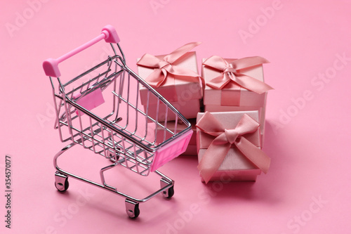 Supermarket trolley with gift boxes on pink pastel background