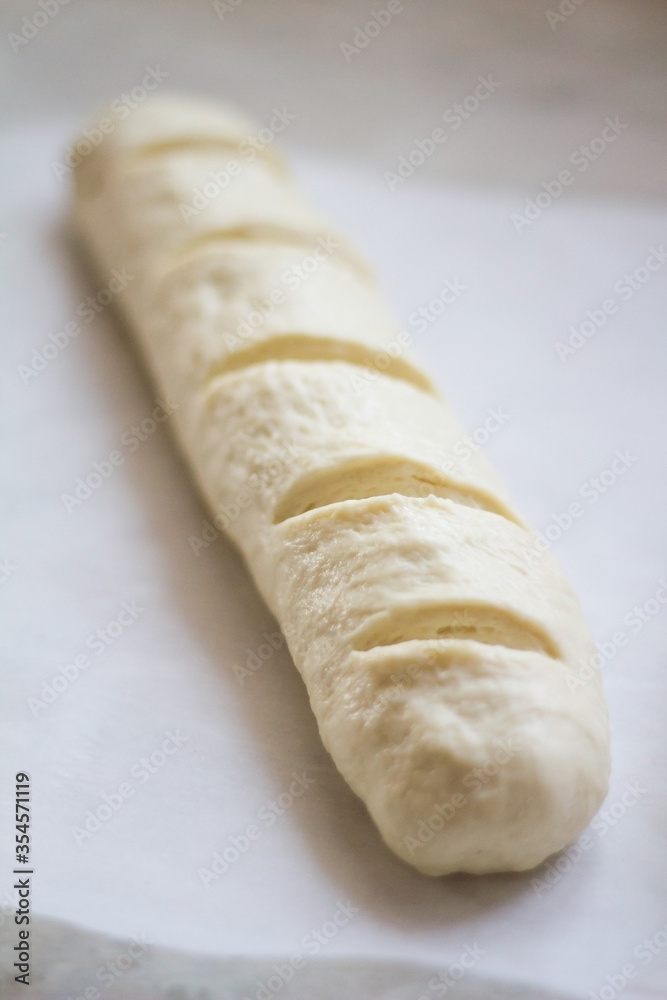 Formed yeast dough for long loaf bread with scores before baking on oven-tray