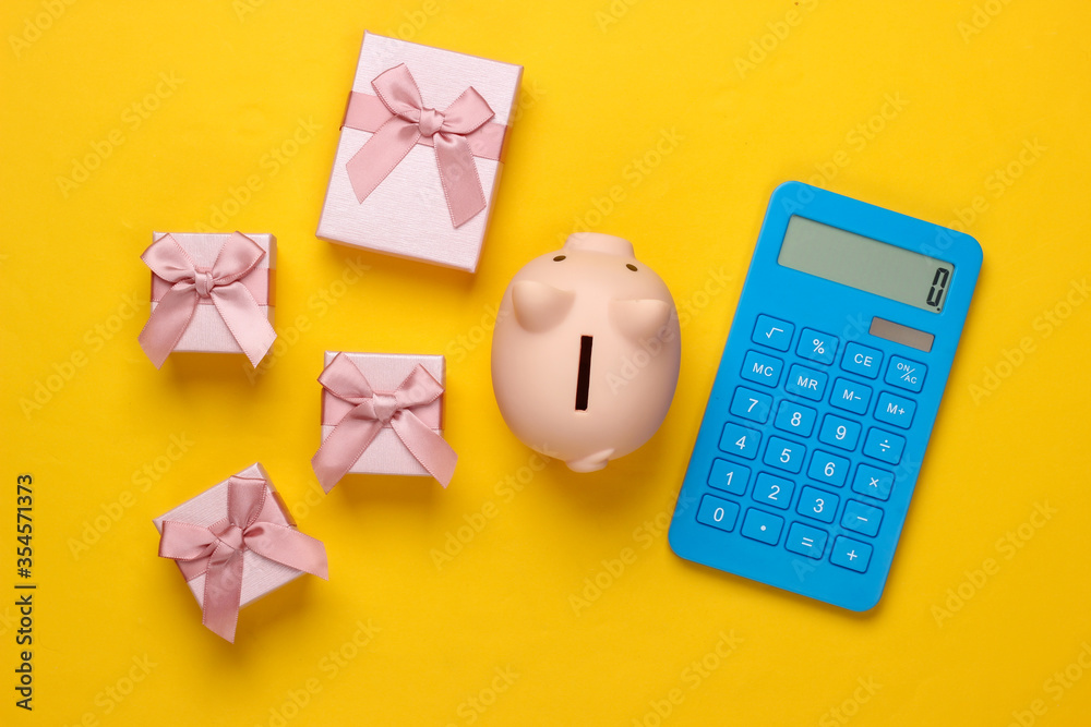 Piggy bank and gift boxes, calculator on yellow background. Minimalistic studio shot. Overhead view. Flat lay. Piggy bank and gift boxes, calculator on yellow background. Minimalistic studio shot. Overhead view. Flat lay.