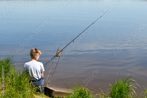 boy child fisherman sits on shore and looks at float. Fishing with children