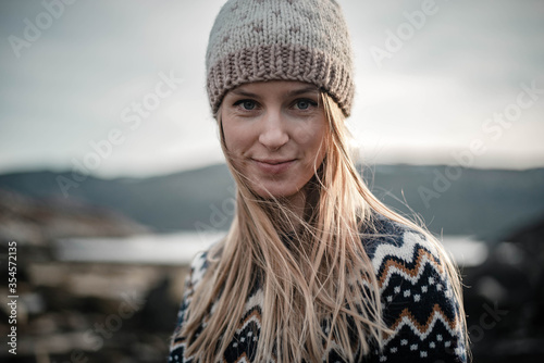 Nice close portrait of a young blodne woman smiling to a camera wearing a handmade knitted hat on a nice sunny spring evening