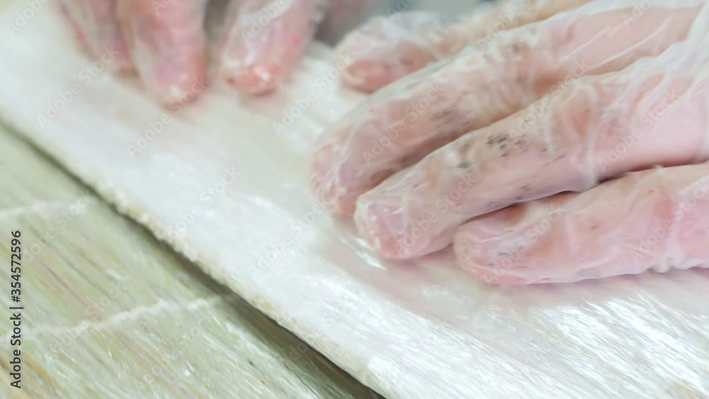 Man in gloves is making a sushi roll with black rice using bamboo mat. Closeup view of process of cooking sushi Man in gloves is making a sushi roll with black rice using bamboo mat. Closeup view of process of cooking sushi