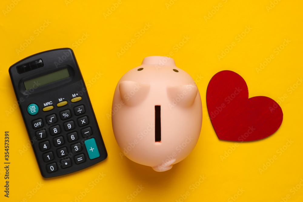Piggy bank, calculator and heart on yellow background. Minimalistic studio shot. Overhead view. Flat lay.