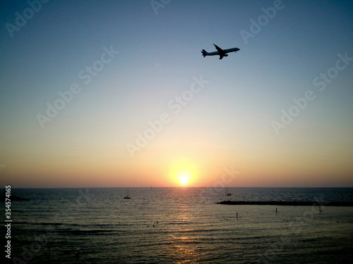 Silhouette of plane flying over Tel Aviv beach at sunset. Golden sky and sea