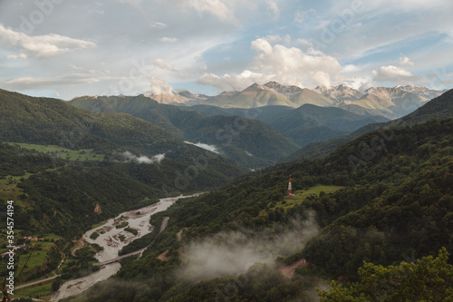 View of the gorge with road, bridge over the Teberda River, green forests on the slopes, high mountains in and cloudy sky, the Caucasus