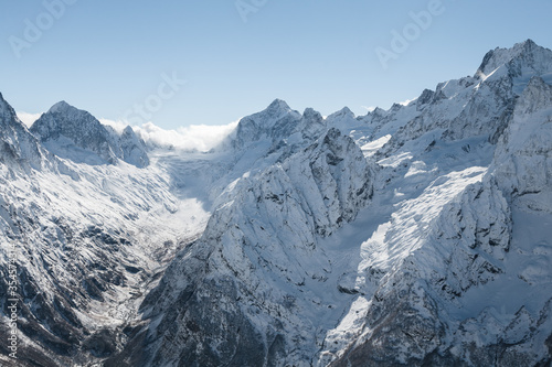 Horizontal landscape with glaciers and peaks of high Caucasus mountain range in Teberda Nature Reserve near Dombay Ski Resort at sunny winter day