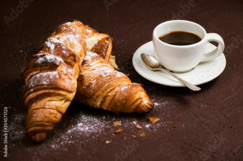 Still life with cup of fresh coffee and delicious butter croissants on dark brown board