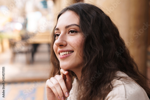 Image of woman looking aside and smiling while sitting in street cafe