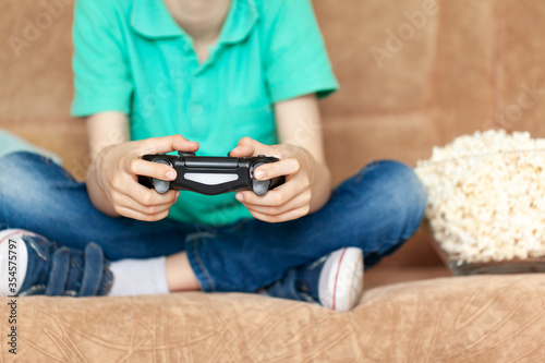 Child playing online video games and eating popcorn sitting on sofa in living room at home. Gaming video games concept