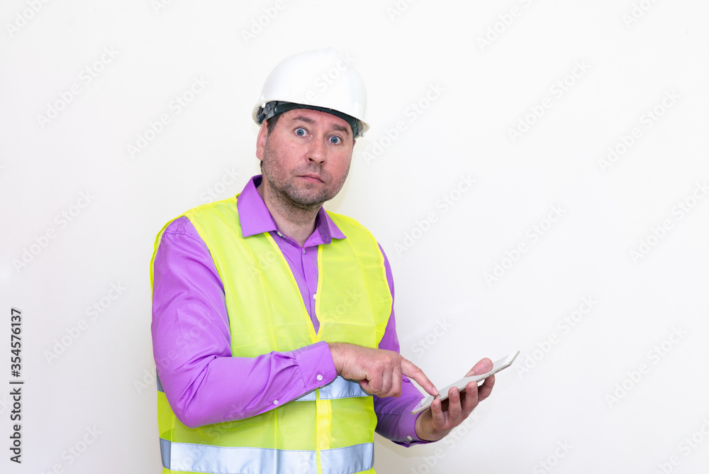 Construction builder wearing helmet yellow protective vest using wireless tablet and showing like or thumbs-up shocked poke up shows to you and victory gesture isolated on white background. Construction builder wearing helmet yellow protective vest using wireless tablet and showing like or thumbs-up shocked poke up shows to you and victory gesture isolated on white background.