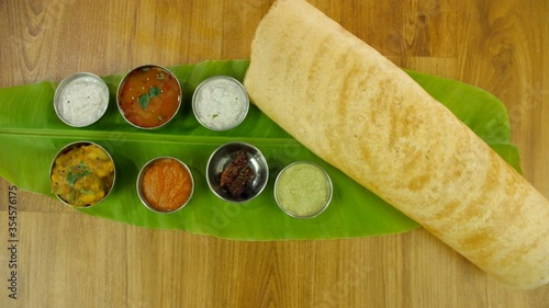 Zoom out shot of South Indian dish masala dosa served over a fresh banana leaf. Top view shot of South Indian breakfast meal dosa with bowls of sambhar  fried red chilly and colorful chutneys photo