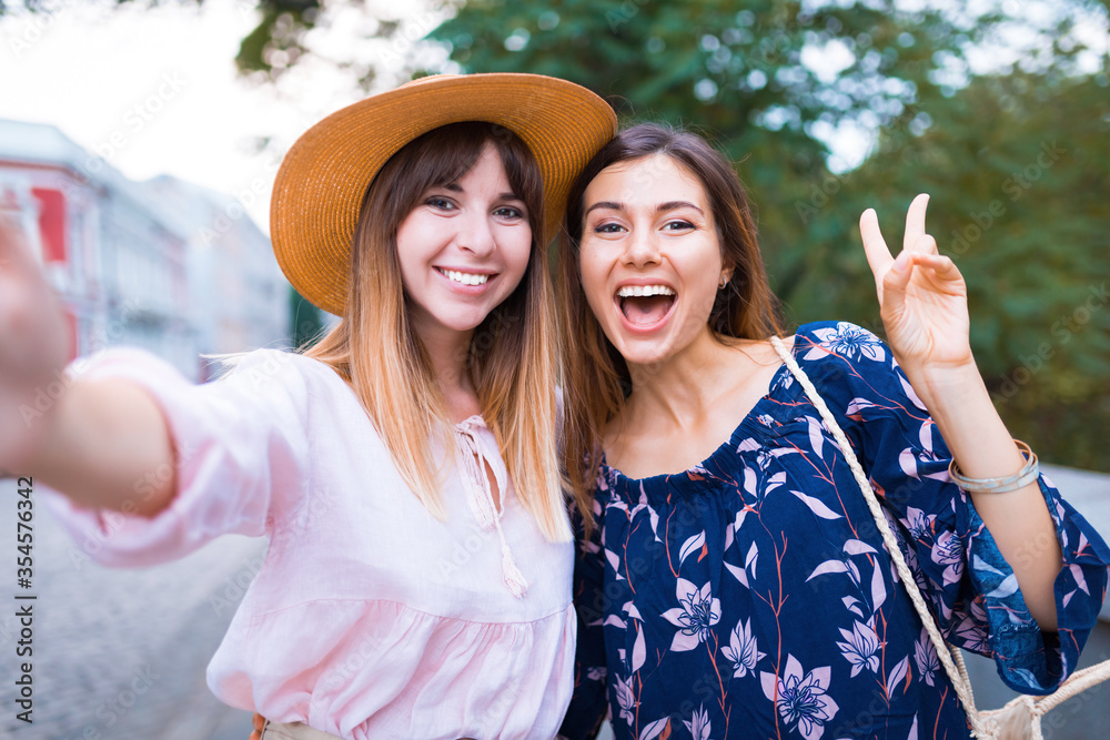 Close up lifestyle selfie portrait of two young positive woman having fun and making selfie, teenage hipster trendy clothes and hats, long hairs,fresh make up. happy together. sisters, friends