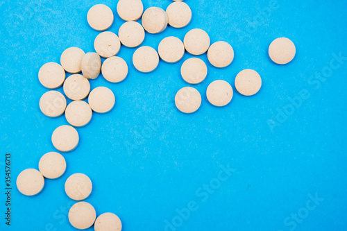 Round white, yellow pills on a blue background top view, side view in macro. Place for text. The tablets lie chaotically on the right, on the left in the middle. Pills in macro