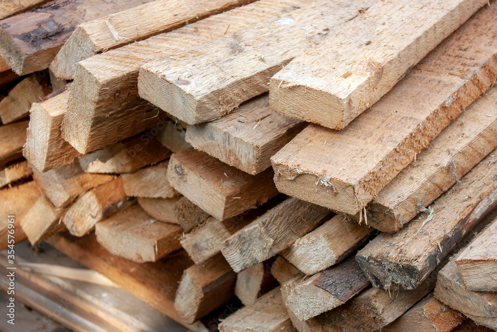 Roughly processed boards lie in a stack. Close-up view of the ends of the boards. Softwood lumber in a stack in the sun. Roughly processed boards lie in a stack. Close-up view of the ends of the boards. Softwood lumber in a stack in the sun.