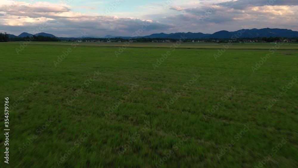 Drone aerial rotating forward low flying over freshly harvested cut grass farming field in the countryside after dusk with mountains and clouds in the distance. Drone aerial rotating forward low flying over freshly harvested cut grass farming field in the countryside after dusk with mountains and clouds in the distance.