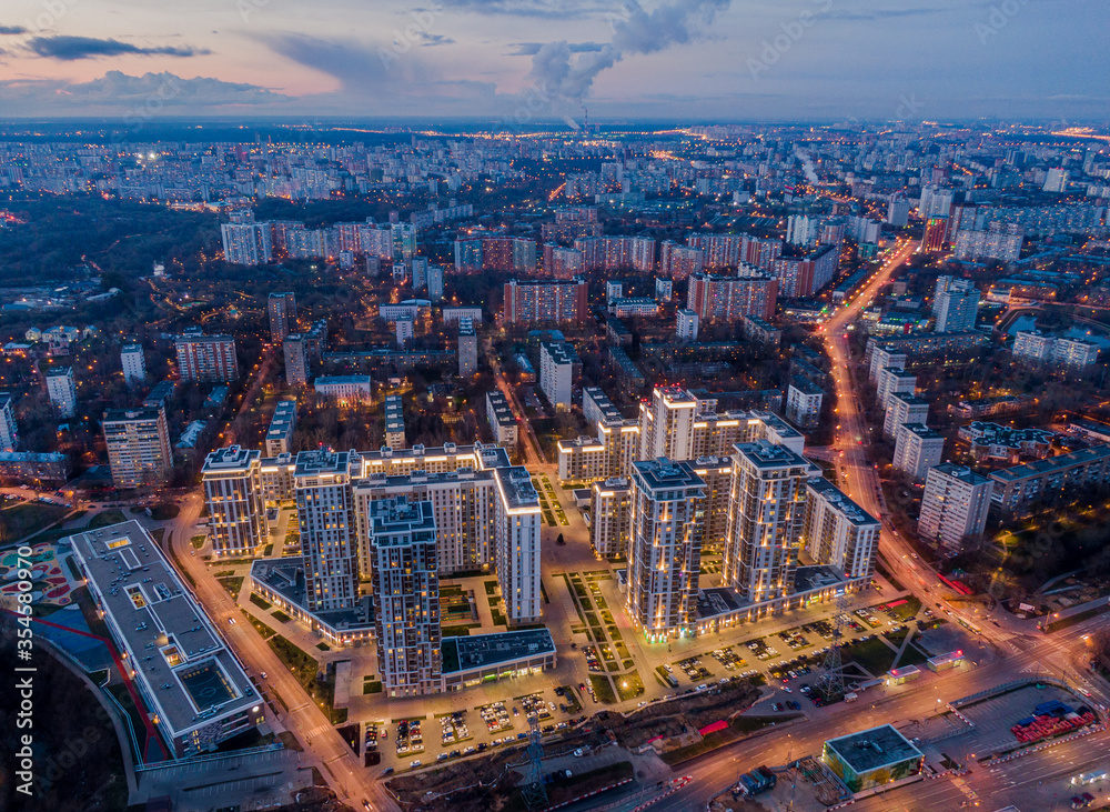 Modern houses with backlight on the background of the night city, in the frame high-rise buildings and old buildings, aerial photography