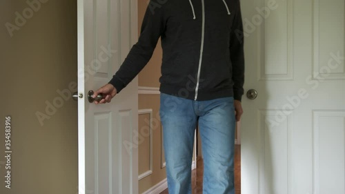 High quality slow motion close-up 4k video of a young man walking into the room on the second floor of his beautiful house. Opening double doors into the bedroom and wearing blue jeans and hoodie.