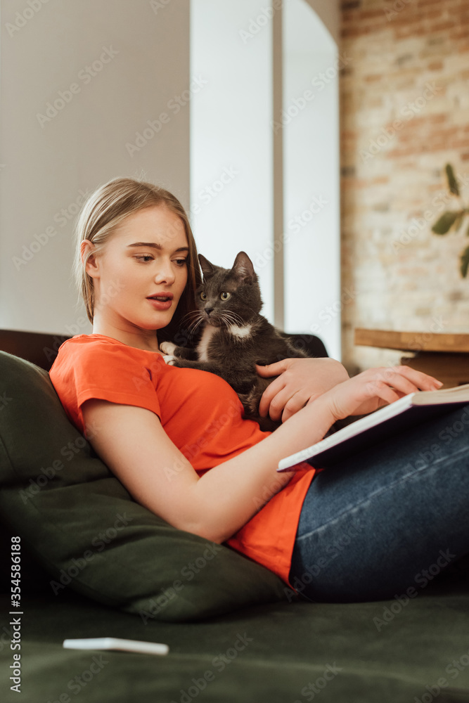 selective focus of beautiful girl holding cat and reading book in living room selective focus of beautiful girl holding cat and reading book in living room