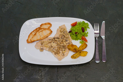 Stewed mushrooms with fish fillet, salad, fried potatoes and croutons, on a warm gray background. Tasty traditional italian food