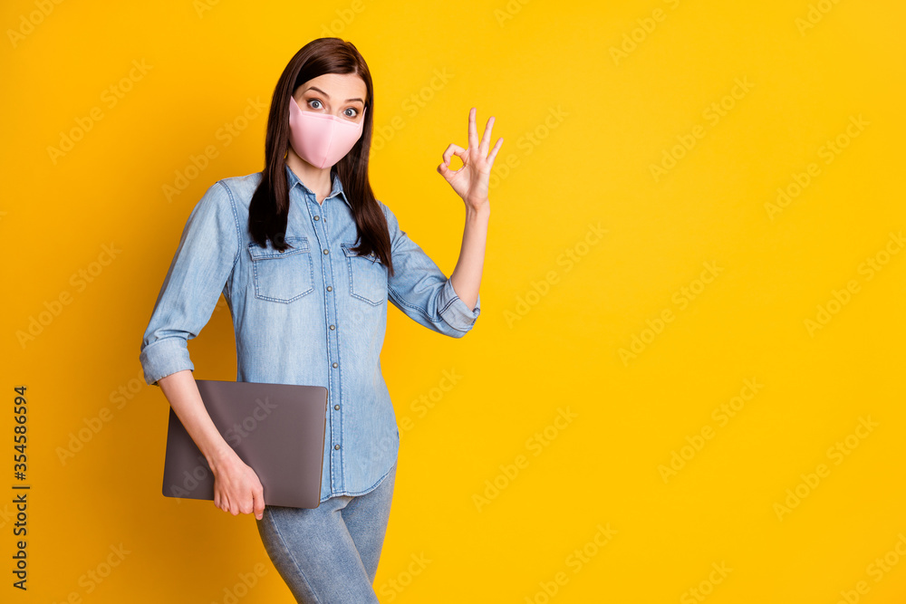 Photo of shocked student girl hold laptop show okay sign approve connection wear medical mask denim jeans shirt isolated over yellow color background Photo of shocked student girl hold laptop show okay sign approve connection wear medical mask denim jeans shirt isolated over yellow color background