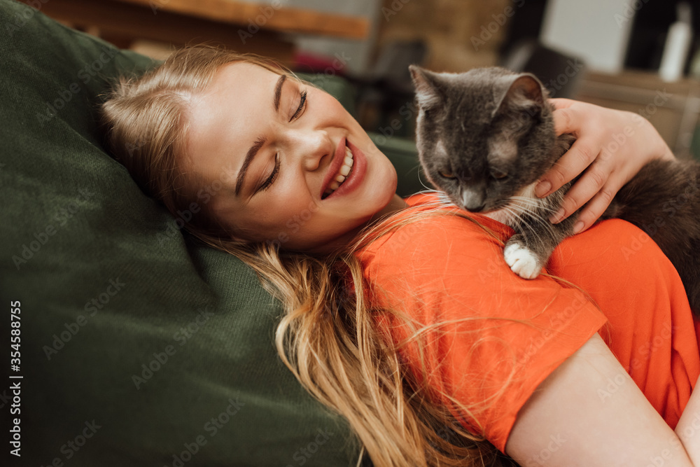 cheerful young woman looking at cute cat in living room