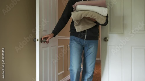High quality slow motion close-up 4k video of a young man walking into the room on the second floor of his beautiful house and holding bath towels. Young man carrying laundry into the closet 
