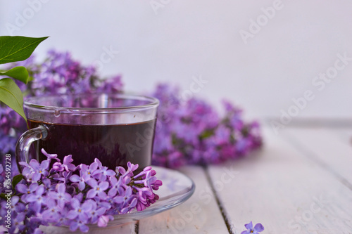 Cup of tea with lilac flowers on a wooden white background. Mocap for postcards. Spring time. Vase with lilacs. Copy space for text. The concept of holidays and good morning wishes