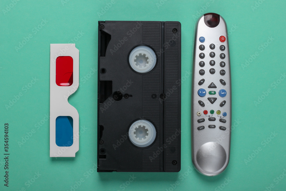 Anaglyph disposable paper 3d glasses, tv remote and video cassette on mint green background. Retro media, entertainment 80s. Top view Anaglyph disposable paper 3d glasses, tv remote and video cassette on mint green background. Retro media, entertainment 80s. Top view