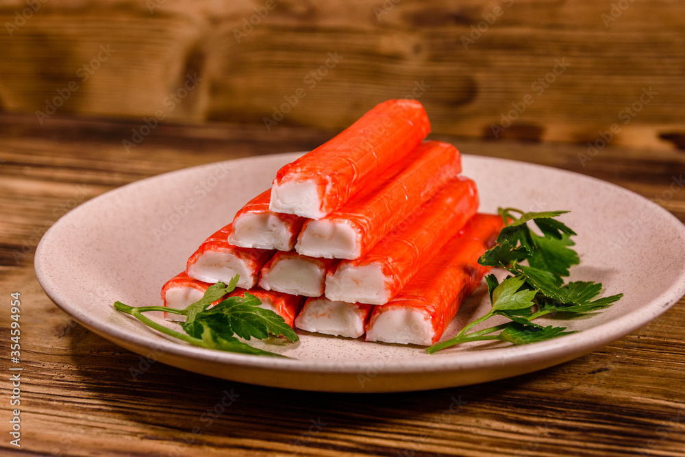 Ceramic plate with pile of crab sticks and parsley twig on a wooden table Ceramic plate with pile of crab sticks and parsley twig on a wooden table