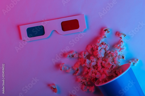 ovie time. Cardboard bucket of popcorn and Stereoscopic anaglyph disposable paper 3d glasses in pink blue gradient neon light. Top view photo