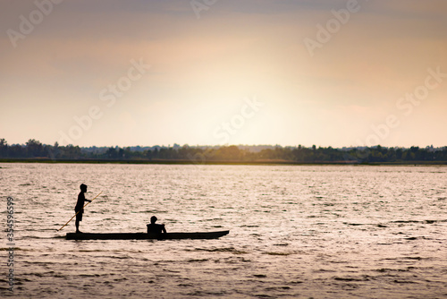 Silhouette image of two boys on a small boat for fishing in the evening.