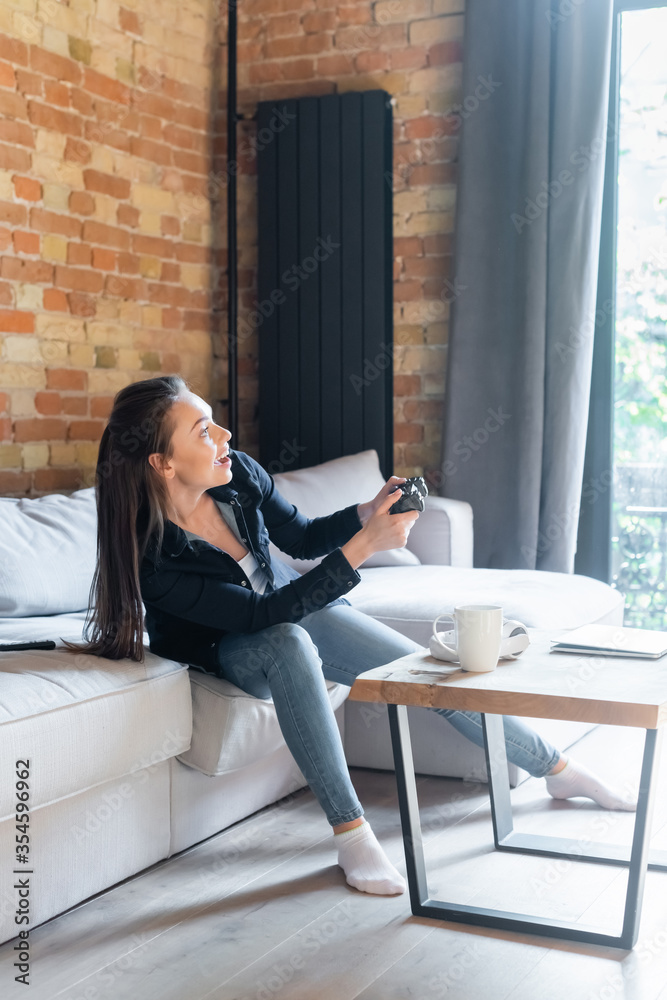 KYIV, UKRAINE - APRIL 29, 2020: happy young woman holding joystick while playing video game in living room KYIV, UKRAINE - APRIL 29, 2020: happy young woman holding joystick while playing video game in living room