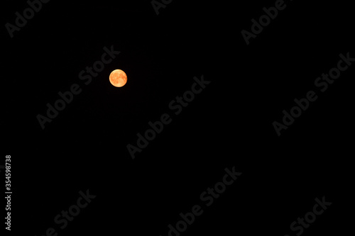 round full moon yellow reddish on a large area of black sky, black background with lots of free space