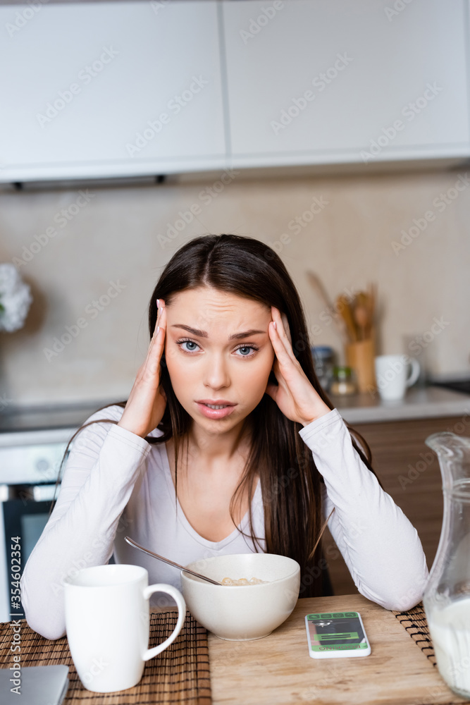 upset girl touching head near bowl, jug and smartphone with booking app upset girl touching head near bowl, jug and smartphone with booking app