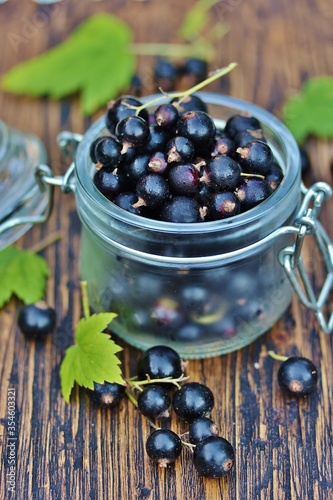 Black currant in a glass jar on a wooden table, against a background of nature. Eco-friendly product. Organic. Favorite French "cassis et groseille"