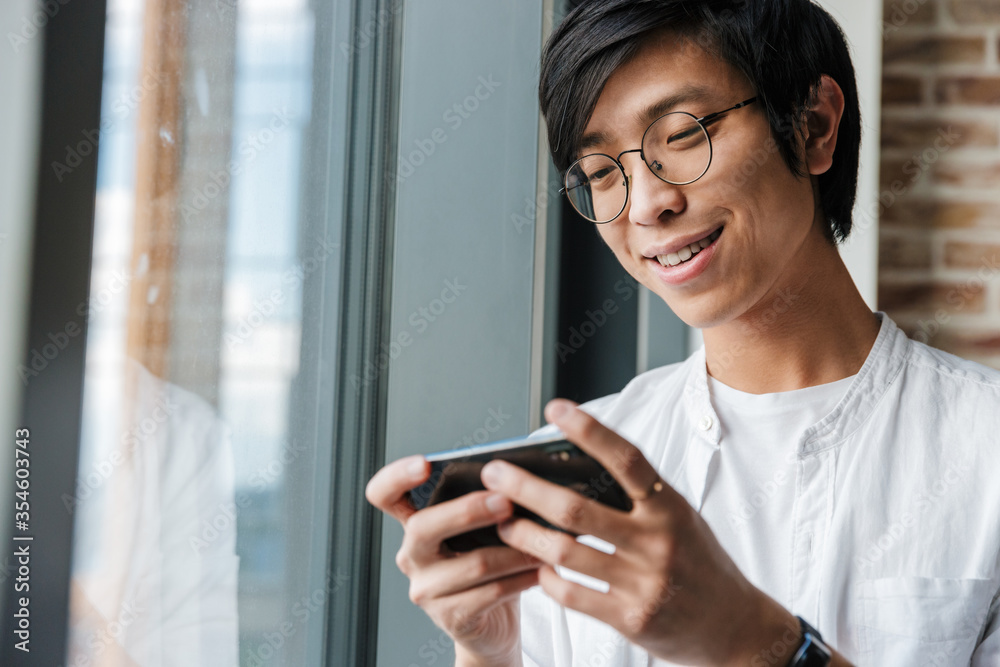 Image of handsome young asian man holding cellphone in office Image of handsome young asian man holding cellphone in office