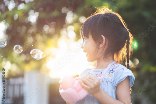Beautiful 4 years old asian little girl is smiling with happy moment while she is playing bubbles outdoor.