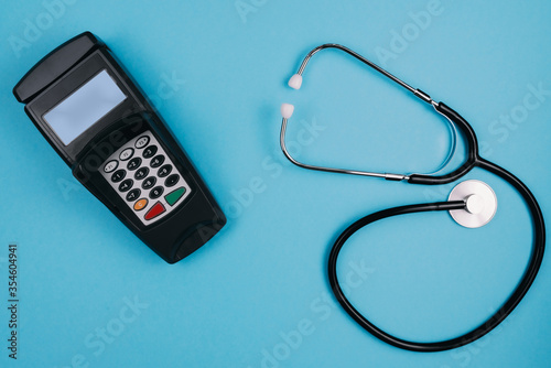 cost and payment for medical treatment or copay concept, above shot of stethoscope and credit card reader on blue desk background photo