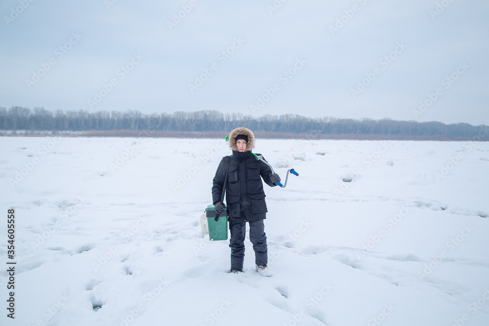 fisherman with a box and an ice drill in winter on ice