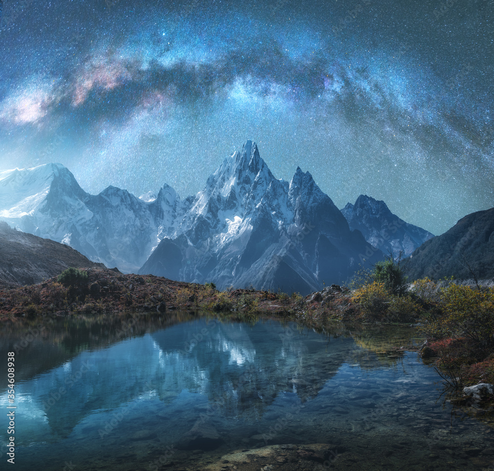 Plakat Milky Way over snowy mountains and lake at night. Landscape with snow covered high rocks and starry sky reflected in water in Nepal. Sky with stars. amazing view with bright milky way in Himalayas