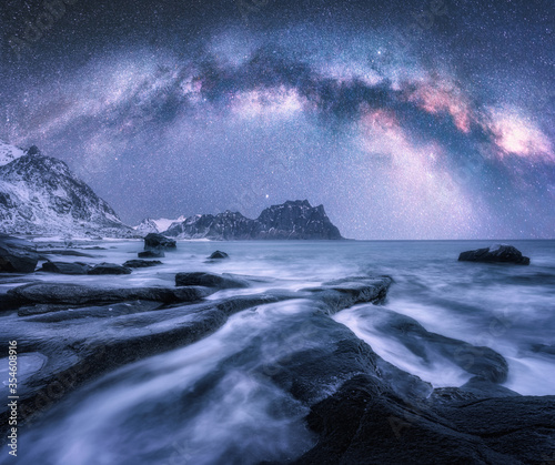 Milky Way over the snow covered mountains and rocky beach in winter at night in Lofoten Islands, Norway. Landscape with purple starry sky, water, stones, snowy rocks, bright milky way. Beautiful space © den-belitsky