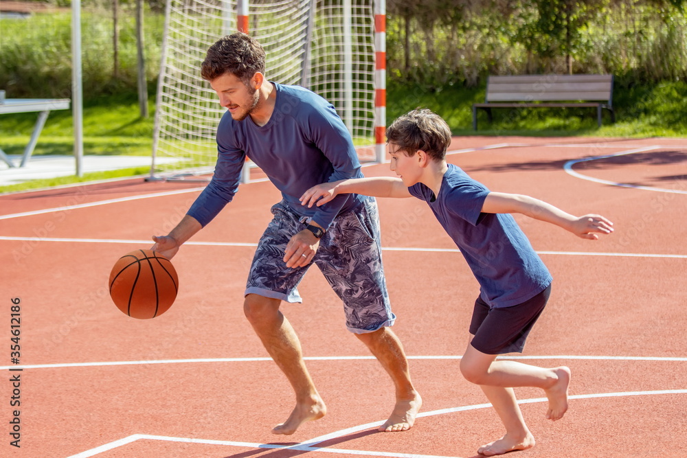 Dad and son playing basketball on a playground