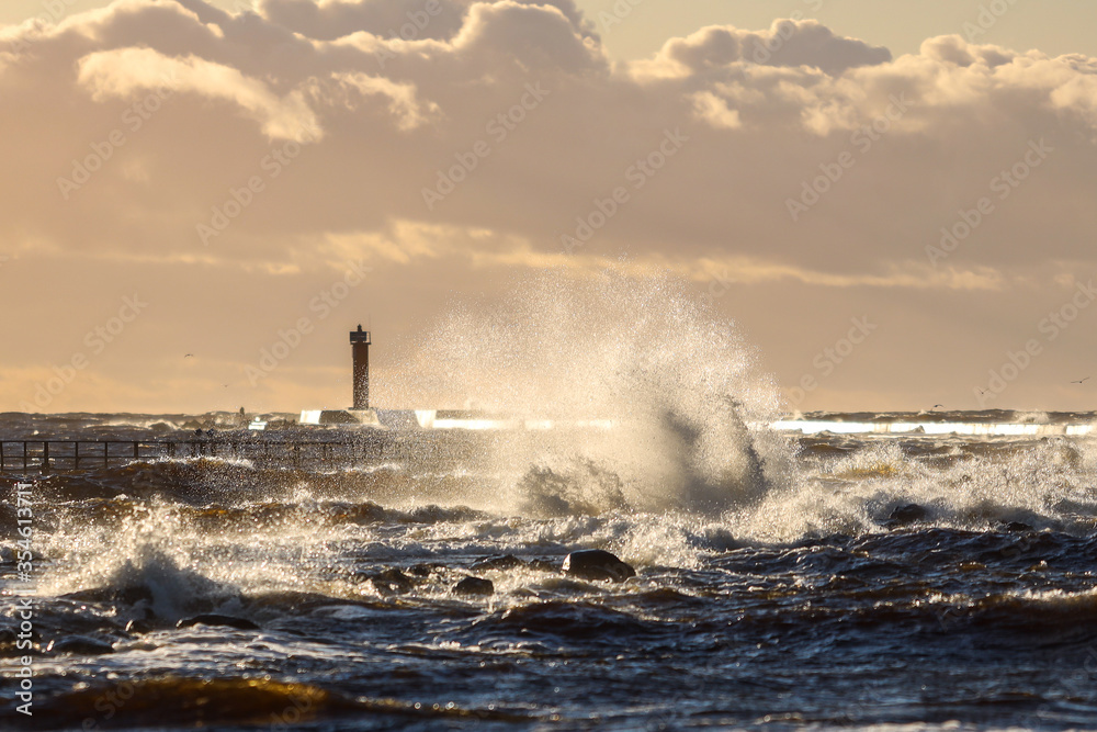 Late sunset view of old lighthouse pier and large storm waves.
