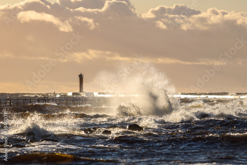 Late sunset view of old lighthouse pier and large storm waves.