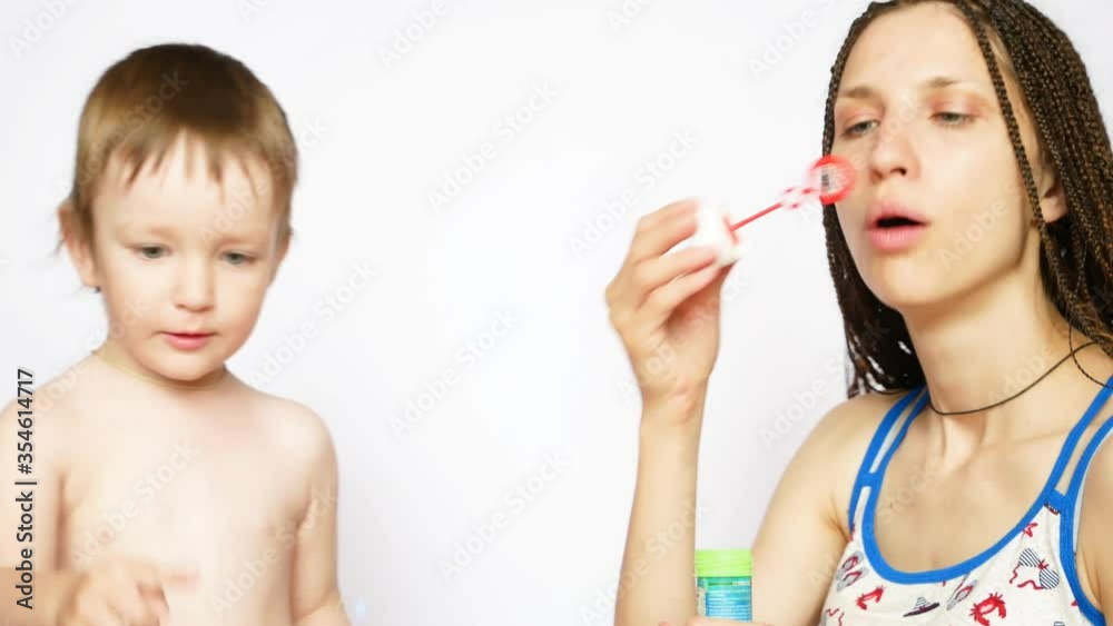 A beautiful braids lady and her little son have fun blowing soap bubbles against white background